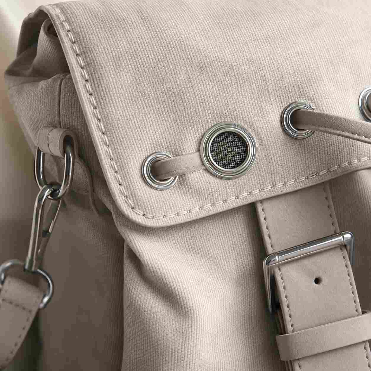 eyelets for bags, Eyelets for bags are installed on the flap of a beige canvas bag to guide straps and provide a mesh-covered opening.
